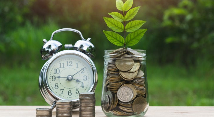 Closeup of an alarm clock and a coin jar with a growing plant symbolizing retirement savings. 